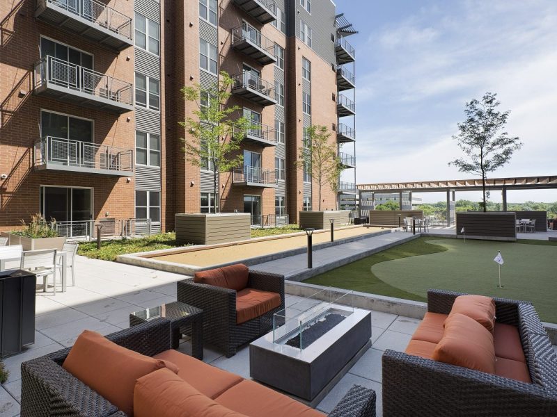 This image shows an expansive view of the Premium Community Amenities, specifically the outdoor fire pit, social lounge, community room, and a spacious putting green for a better fun experience.