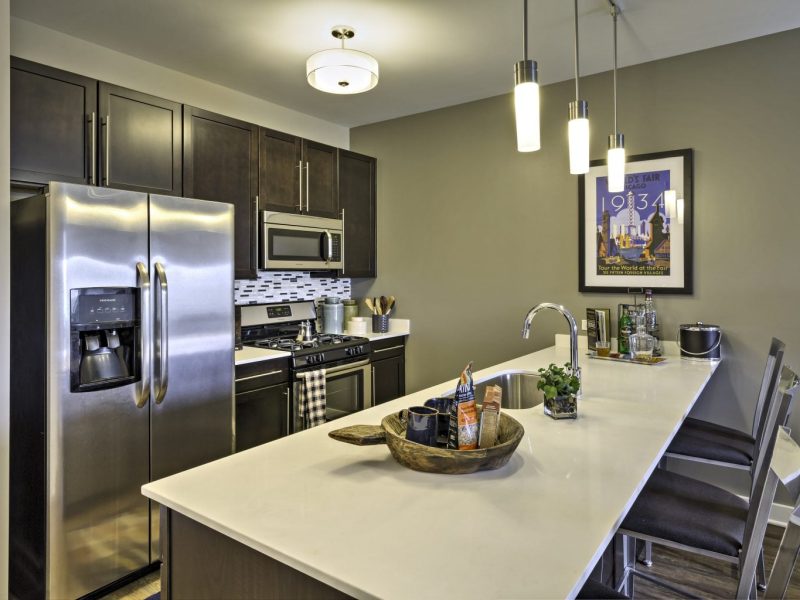This image shows a gourmet open kitchen with a breakfast bar and stunning lights. It features stainless steel appliances and built-in microwaves.